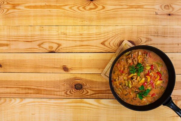 Stew with meat and vegetables in tomato sauce on wooden background. Top view