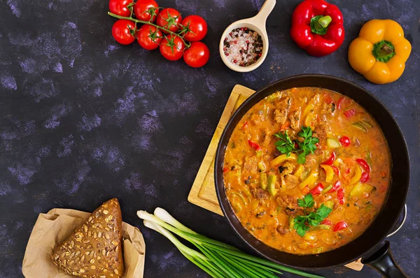 Stew with meat and vegetables in tomato sauce on dark background