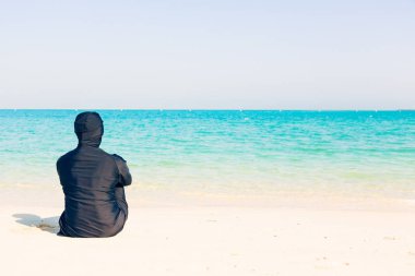 Deniz kenarında oturan Burkini giyen genç kadın
