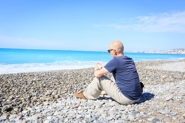 Turista a Niza sentado en la playa, mensajes de texto en su teléfono —  Fotos de Stock