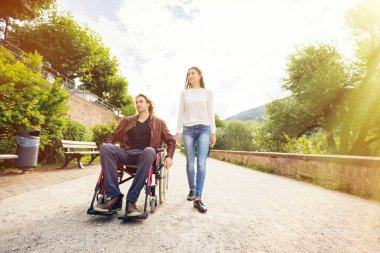 Tekerlekli sandalyede parkta gezen genç bir çift.