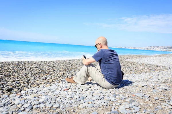 Homem sentado na praia, mensagens de texto em seu telefone — Fotografia de Stock