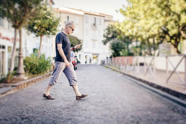 Человек, переходящий улицу и смотрящий на свой телефон — стоковое фото