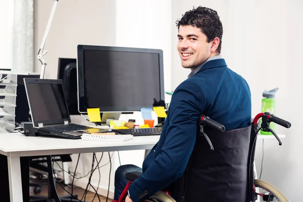 Человек, сидящий в инвалидной коляске, работает в современном офисе — стоковое фото