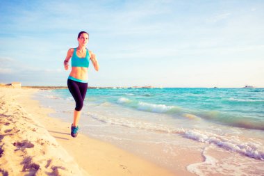Genç bir kadın sahilde koşuyor.