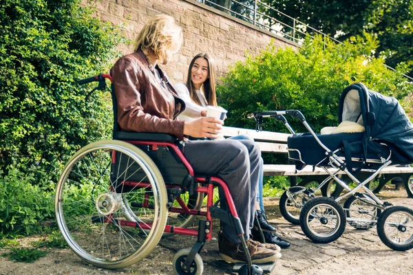 Young Parents In Wheelchair With Baby Stroller In The Park