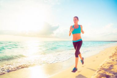 Genç bir kadın sahilde koşuyor.