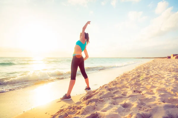 Junge Frau dehnt sich am Strand — Stockfoto