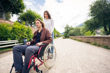 Tekerlekli sandalyede parkta gezen genç bir çift.