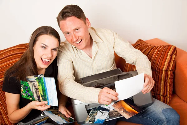 Pareja sentada en el sofá imprimiendo fotos — Foto de Stock