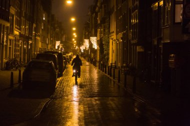 Bicyclist silhouetted by Amsterdam street lights on wet pavement clipart
