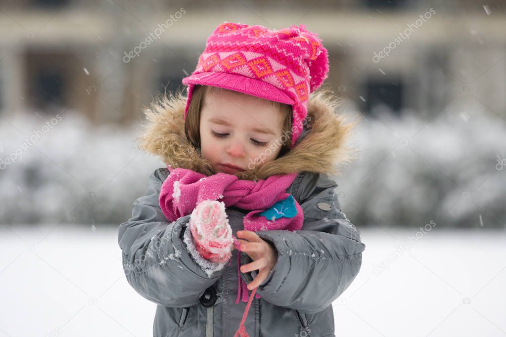 Portrait of a young girl outside in snowy weather dressed in winter clothes, watching snowflakes falling on her gloves