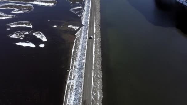Voiture conduisant le long d'une route étroite traversant un lac en Islande 