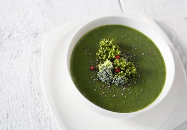 Beyaz kâse içinde brokoli bulunan yeşil ıspanak çorbası beyaz ahşap masa manzaralı. Yemek çizimleri ve diyet makaleleri için uygundur..