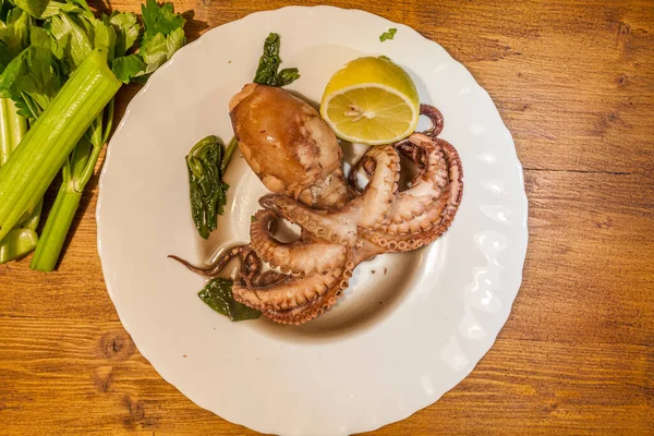 Plate with freshly cooked octopus with celery and lemon, on wooden background