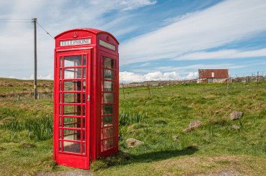 Arkasında küçük bir ev olan izole bir telefon kulübesi.
