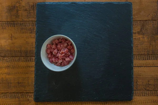 Diced bacon in a white cup on top of a slate plate — Stock Photo, Image