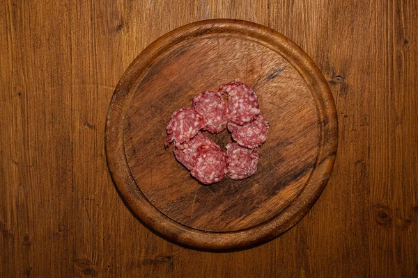 Top view of wooden plate with salami slices — Stock Photo, Image