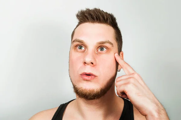 Junger denkender Typ mit Bart in schwarzem T-Shirt hält den Finger am Kopf, auf grauem Hintergrund. — Stockfoto