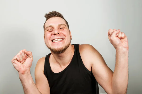 Joven barbudo divertido ganador feliz vestido con camiseta negra levanta las manos con los puños hacia arriba aislado sobre fondo claro . —  Fotos de Stock