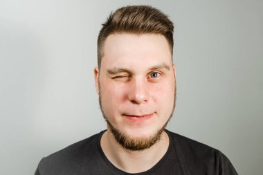 Sakallı, modern saç stili, gri arka planda gülümseyen genç adam..