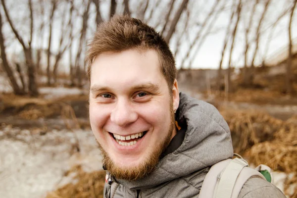 Gengibre jovem cara com barba sorrisos e olha para cima contra o céu, árvores e nuvens . — Fotografia de Stock