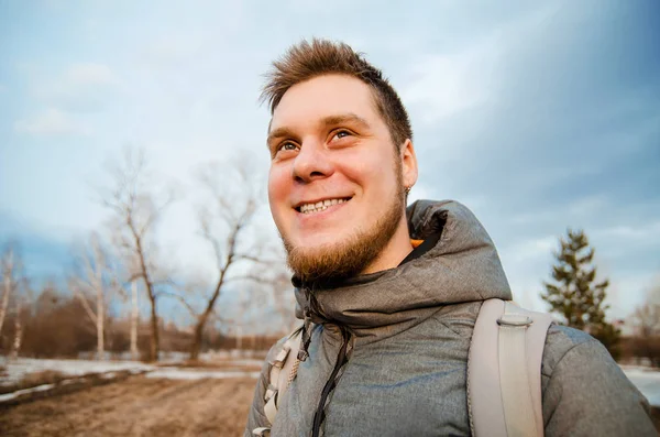 Joven pelirrojo con barba sonríe y mira hacia el cielo, árboles y nubes . — Foto de Stock