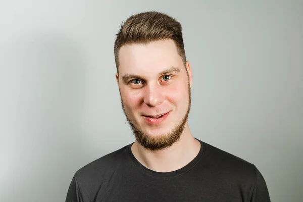 Jeune homme souriant avec barbe et coiffure moderne sur fond gris . — Photo