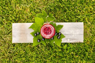 Bir kavanoz siyah kuşüzümü reçeli, yeşil çimenlerin arka planında, ahşap bir tahtanın üzerinde.