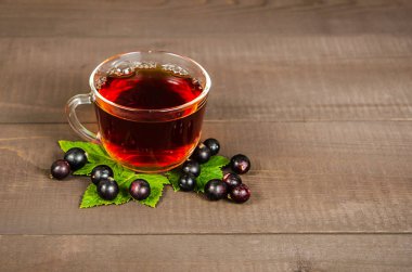 Bir bardak çay fincanı siyah frenk üzümü ve şeker küpleriyle ahşap bir arka planda, bir huş kütüğünün üzerinde duruyor..