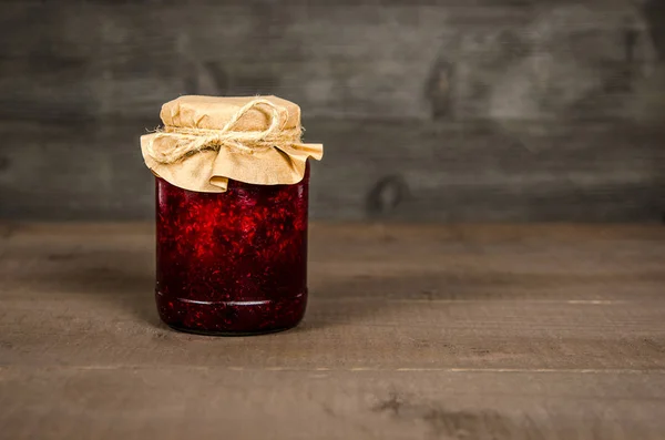 Jar with jam of berries wrapped in wrapping paper, on wooden background — Stock Photo, Image