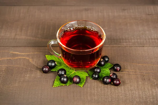 Una taza de té con bayas de grosella negra y terrones de azúcar está sobre un tocón de abedul, sobre un fondo de madera . —  Fotos de Stock