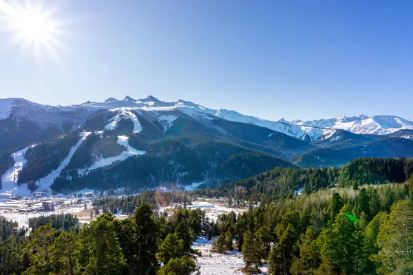 Paesaggio soleggiato invernale con cime innevate di catene montuose con alberi verdi e cielo blu — Foto Stock