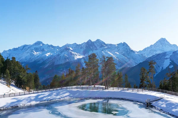 Paesaggio soleggiato invernale con cime innevate di catene montuose con alberi verdi e cielo blu — Foto Stock