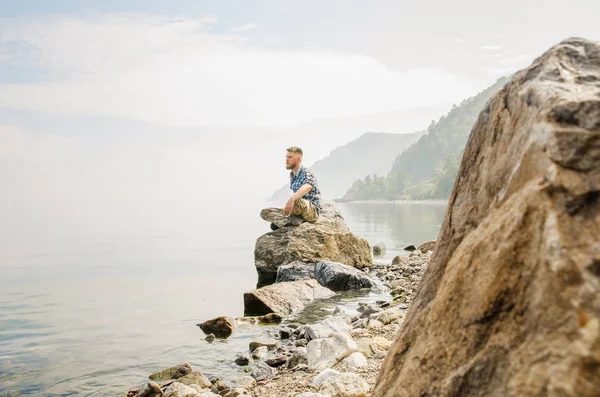 젊은 남자가 배낭을 찬 채 호수와 산을 배경으로 여행하는 모습 — 스톡 사진