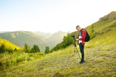Fotoğrafçının eli kamerayı tutuyor ve doğada kayanın üstünde duruyor. Seyahat kavramı.