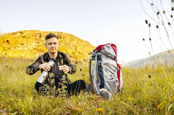 Hipster jovem com mochila desfrutando do pôr do sol no pico da montanha . — Fotografia de Stock