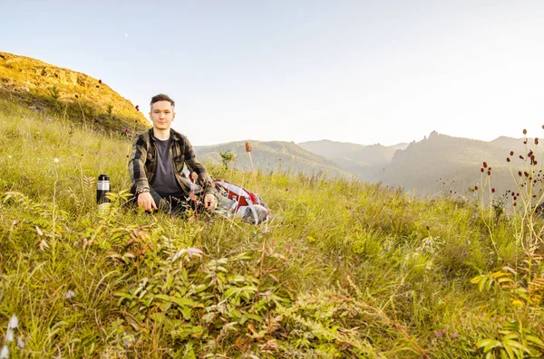 Hipster joven con mochila disfrutando de la puesta del sol en la montaña pico . — Foto de Stock