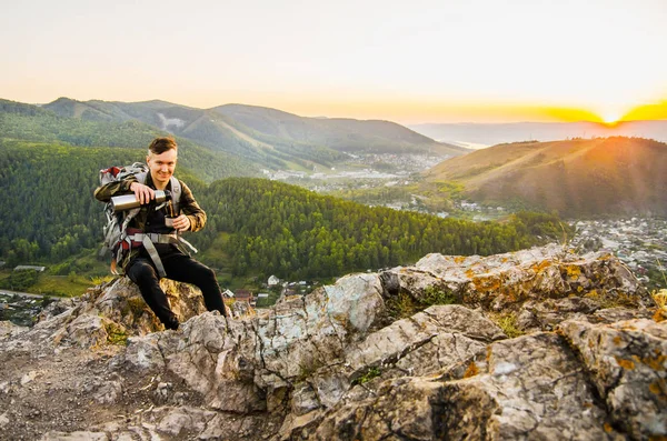 Hipster joven con mochila disfrutando de la puesta del sol en la montaña pico . — Foto de Stock