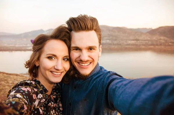 Par i kärlek glada promenader och omfamna på floden bakgrund — Stockfoto