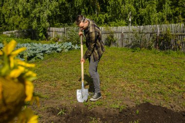 Genç adam elinde kürekle bahçeyi kazıyor.