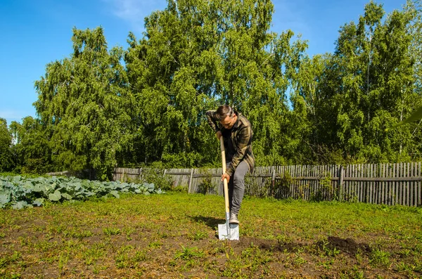 Jovem cavou o chão no jardim com uma pá — Fotografia de Stock