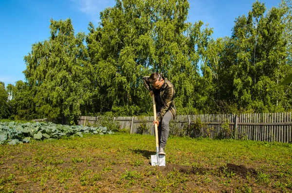 Jeune homme creuse le sol dans le jardin avec une pelle — Photo