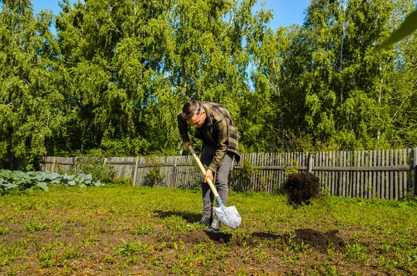 Jeune homme creuse le sol dans le jardin avec une pelle — Photo