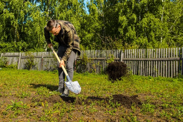 Jeune homme creuse le sol dans le jardin avec une pelle — Photo