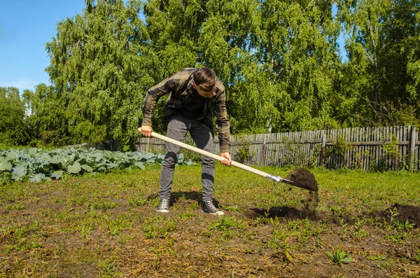Young guy digs the ground in the garden with a shovel — Stock Photo, Image