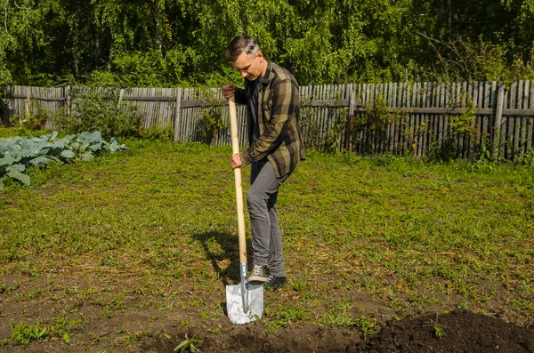 Ung kille gräver marken i trädgården med en spade — Stockfoto