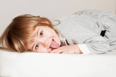 Küçük kız yerde oturuyor ve dilini gösteriyor..