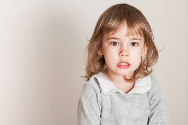 Hafif bir arka planda, ciddi yüzlü, üzgün küçük bir kızın portresi.