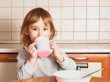 Küçük kız mutfaktaki masada yiyip içiyor.